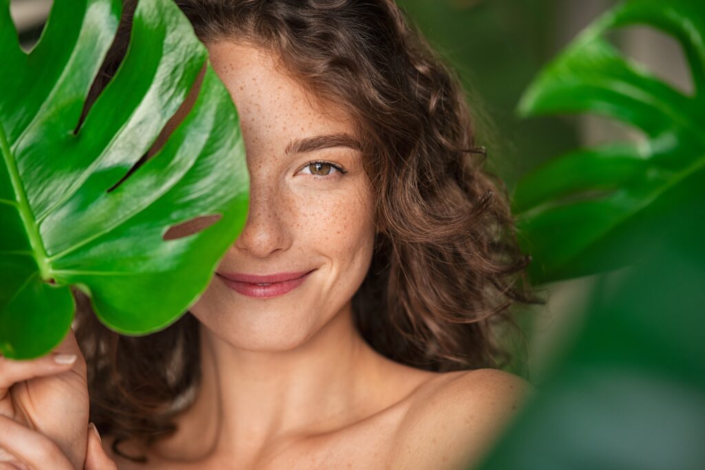 young woman smiling behind a leaf